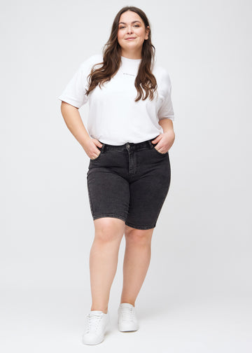 Full image of a plus-size model in dark grey denim skinny middle shorts.