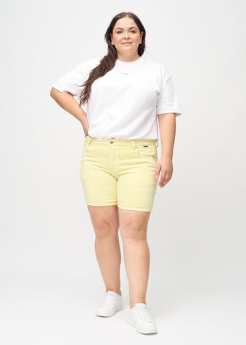 Full image of a plus-size model wearing light yellow skinny short shorts.
