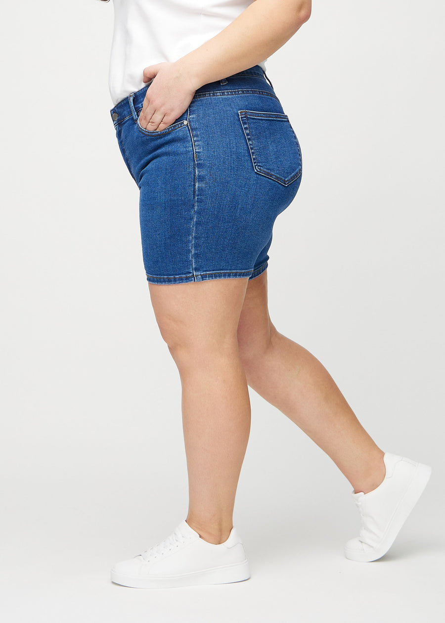 Dark denim skinny short shorts seen from the side on a plus-size model.