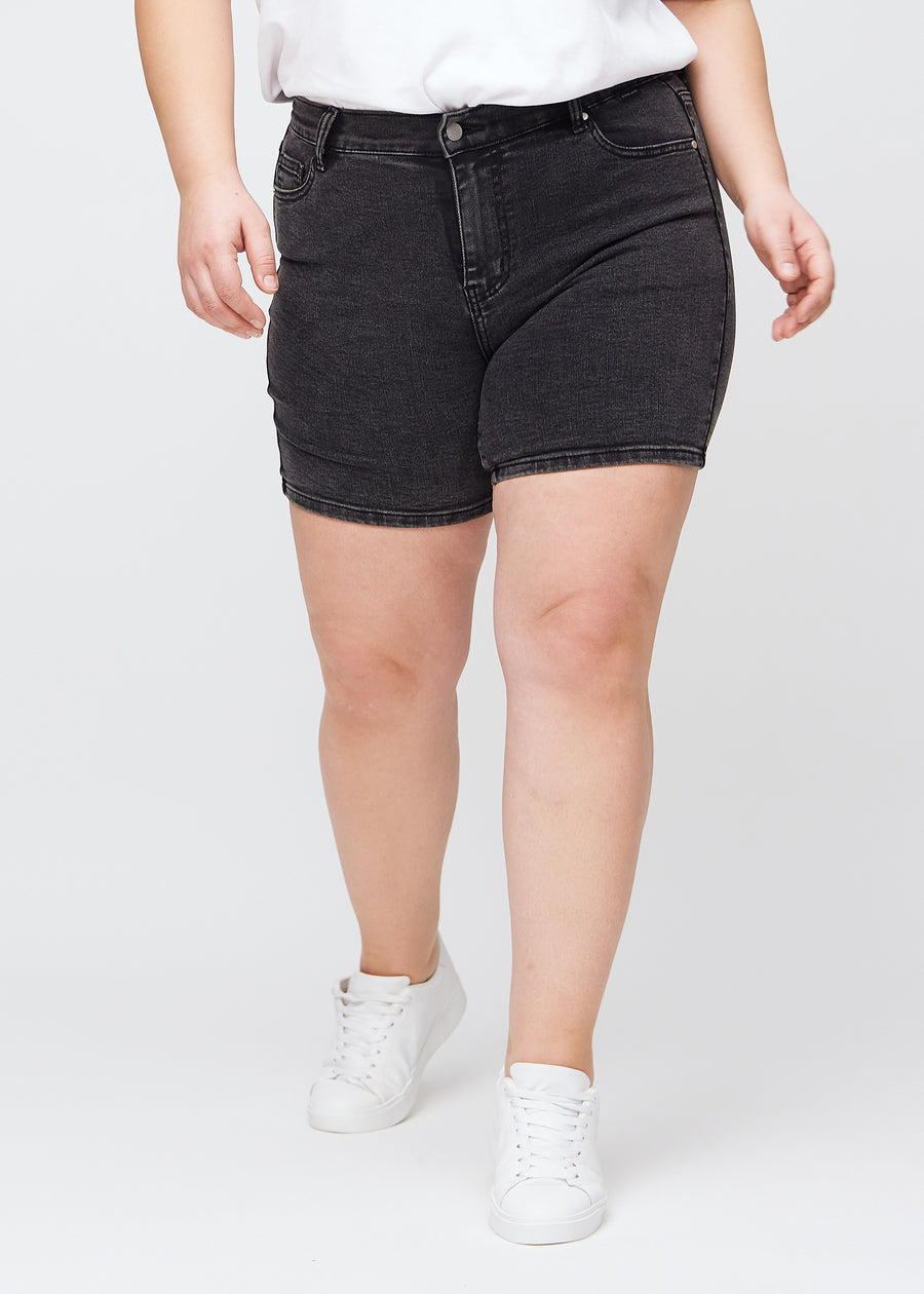 Dark grey denim skinny short shorts, model name Shadows, which are tight-fitting and end mid-thigh on a plus-size model, seen from the front.