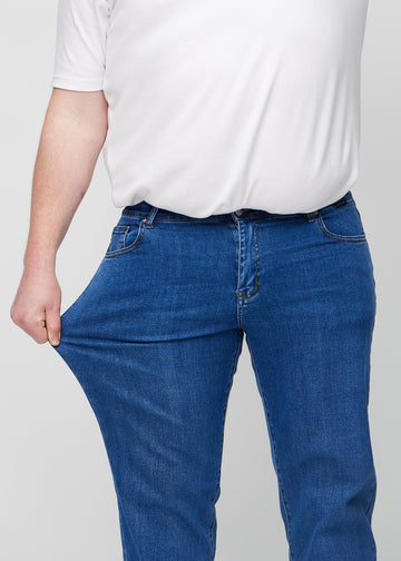 The plus-size model stretches the jeans at the thigh to show the stretch.