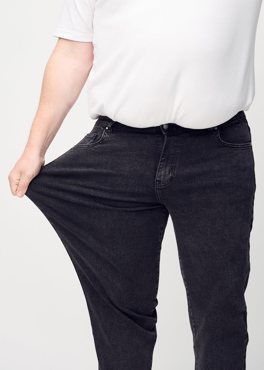 The plus-size model stretches the jeans at the thigh to show the stretch.