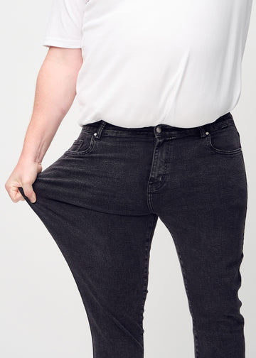 Plus-size model stretches the jeans at the thigh to show the fabric&