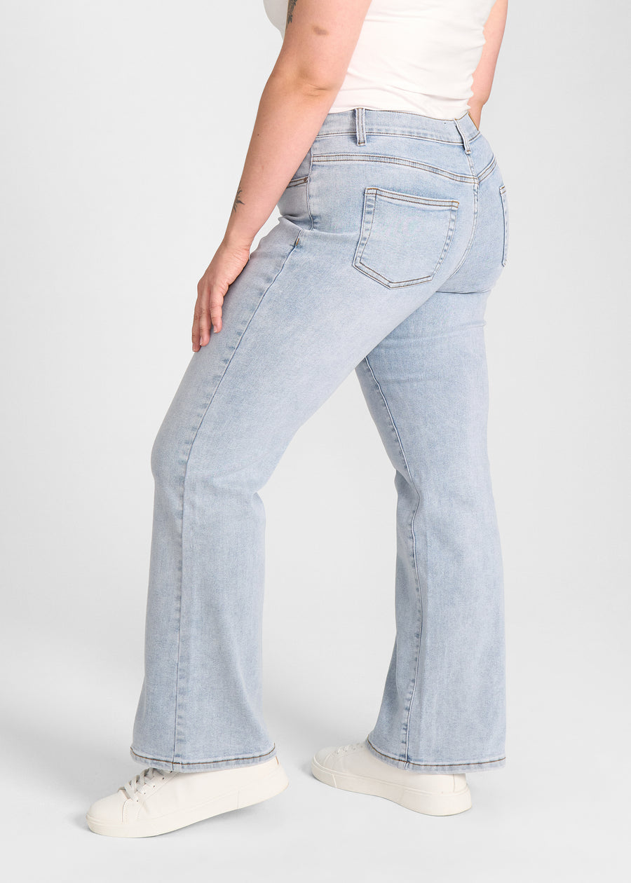 Lyseblå denim bootcut jeans, modelnavn Waves, som sidder tæt om hofter og lår med et let svaj fra knæet og ned, set fra siden på model på en plus-size model.