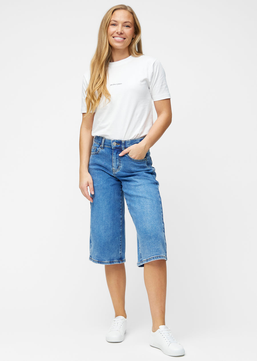 Model viser løse, klassisk blå denim capris i farven Rivers i bevægelse og demonstrerer pasform og materiale.