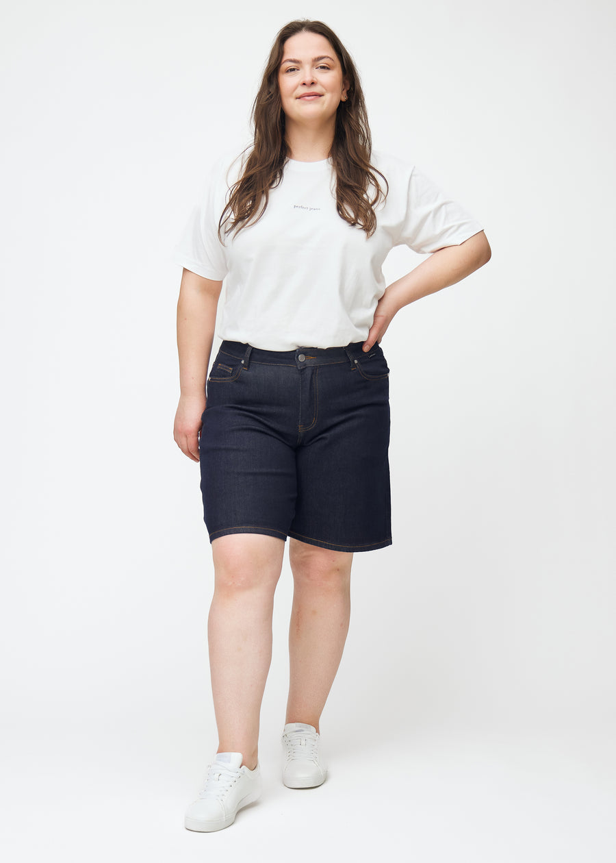 Plus-size model viser dyb mørkeblå denim shorts til kvinder i farven Midnights med loose pasform i bevægelse.