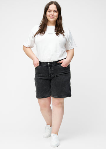 Plus-size model viser løse, mørkegrå denim shorts i farven Shadows i bevægelse og demonstrerer pasform og materiale.
