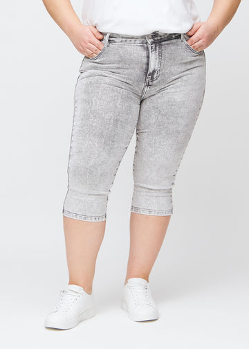 Lysegrå denim skinny capris, modelnavn Ashes, som sidder tæt til benet og slutter lige under knæet på en plus-size model, set forfra.